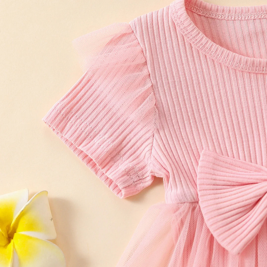 Close-up of pink ribbed short sleeve dress with tulle accents and bow detail on beige background