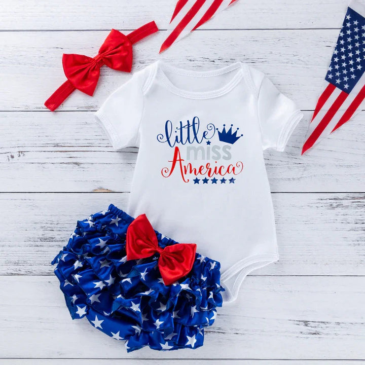 Baby outfit with white onesie reading 'little miss America', blue starry ruffle shorts with red bow, red headband, and small American flags