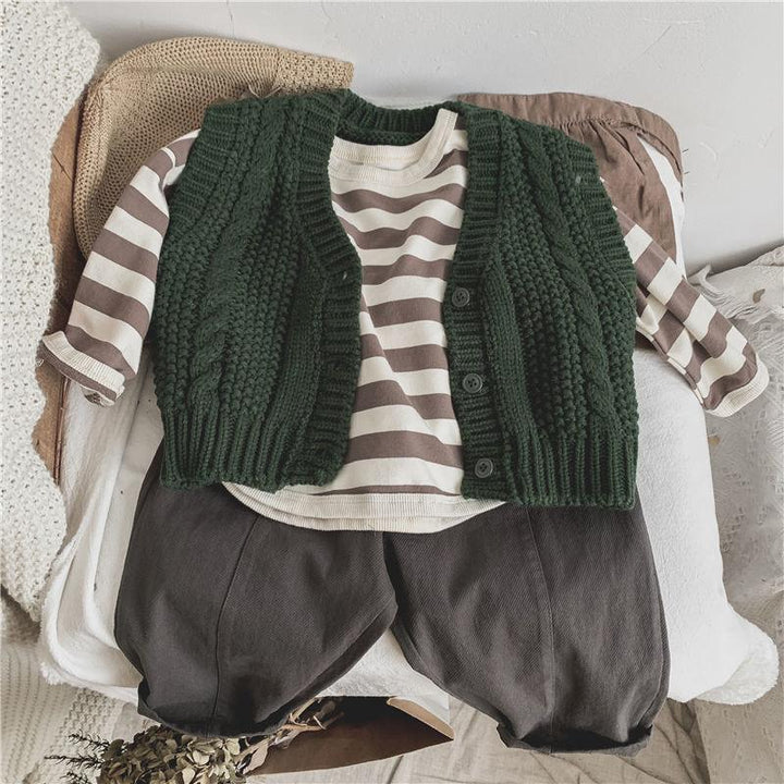 Children's outfit with green knitted vest, striped long-sleeve shirt, and dark pants on a beige chair