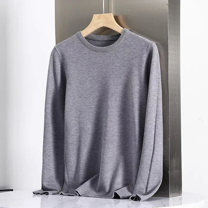Grey long sleeve crewneck sweater on wooden hanger against metallic background