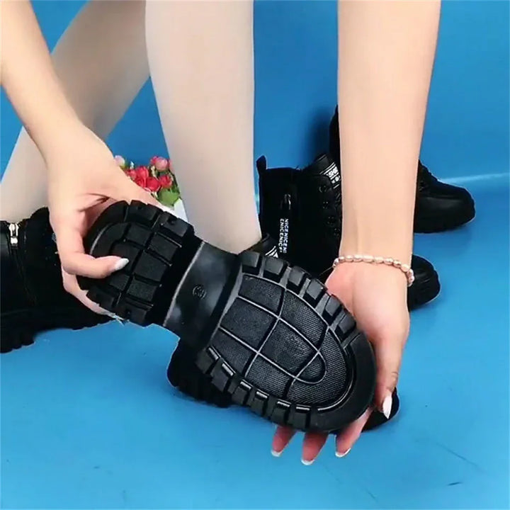 Black chunky sole boots held by hands with pink nail polish on blue background