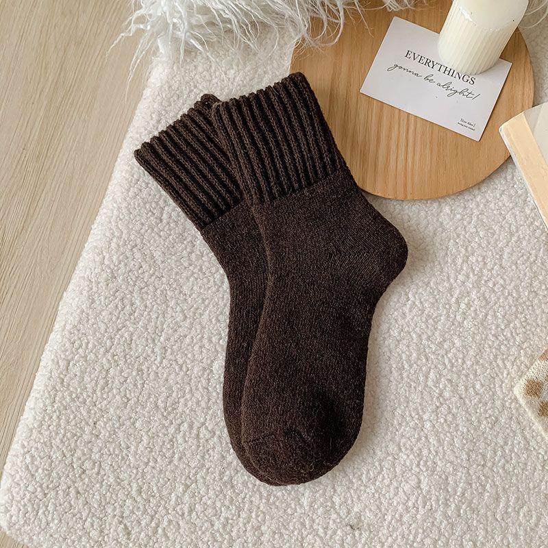 Pair of dark brown cozy wool socks on textured cream fabric with wooden tray and candle