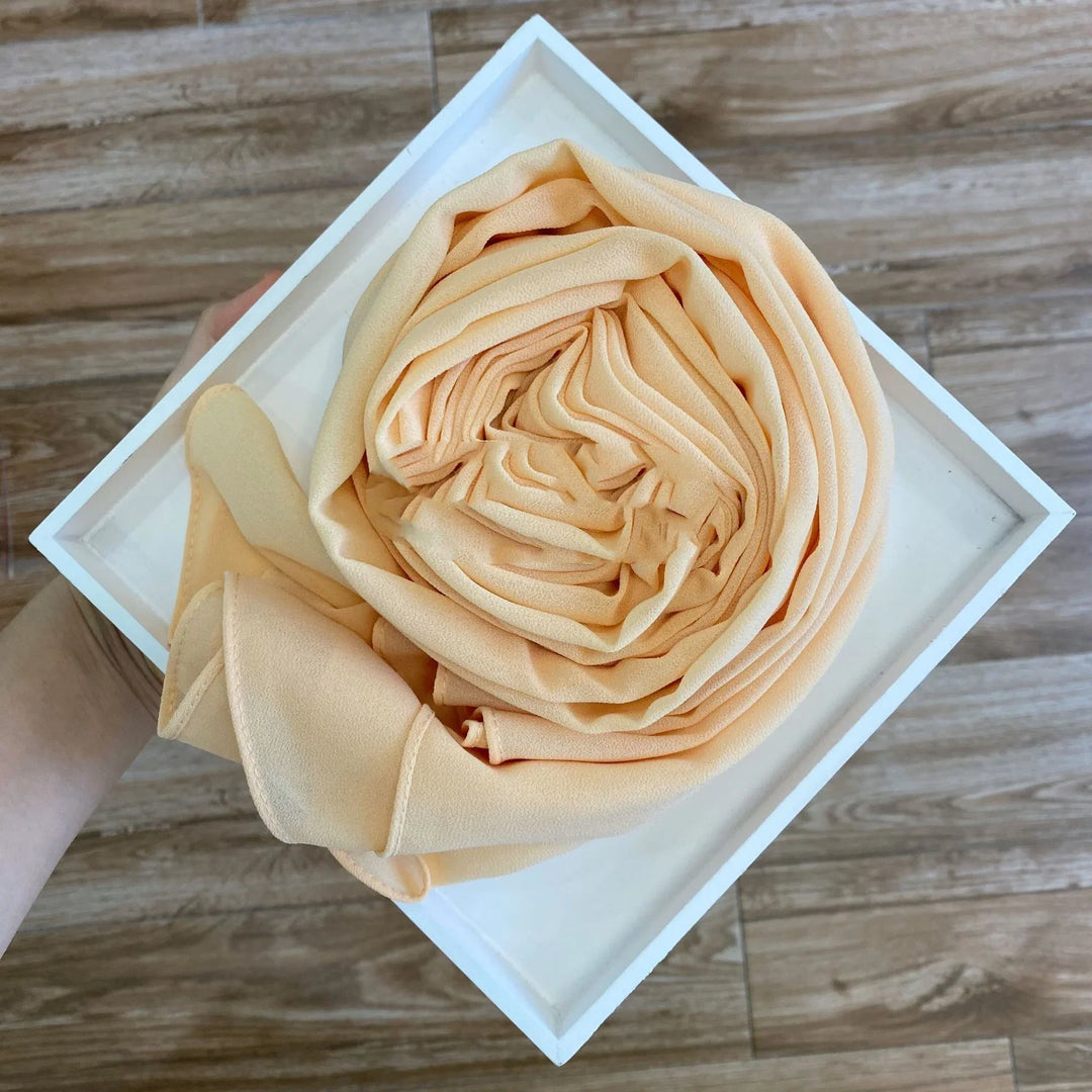 Hand holding white square box with neatly rolled beige fabric inside on wooden floor