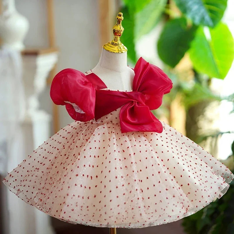Elegant baby dress with red puff sleeves, large bow, and white skirt with red polka dots on mannequin