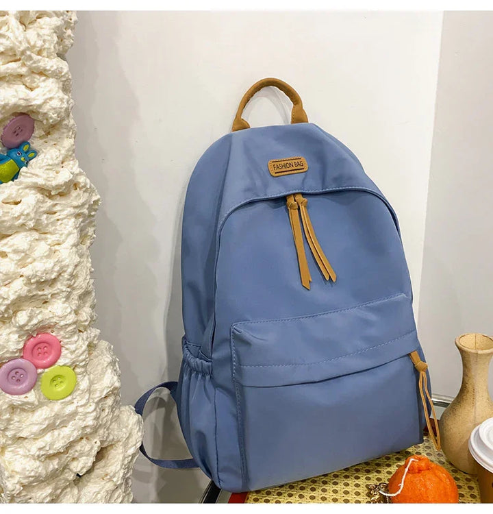 Blue backpack with tan leather accents labeled Fashion Bag, placed on patterned surface against white wall