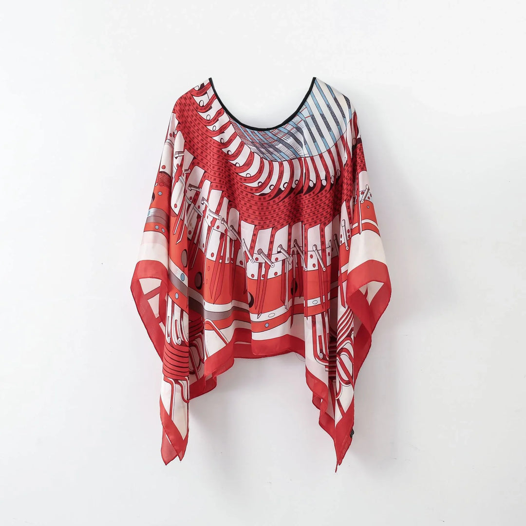 Red and white geometric patterned silk poncho with black trim hanging on white wall