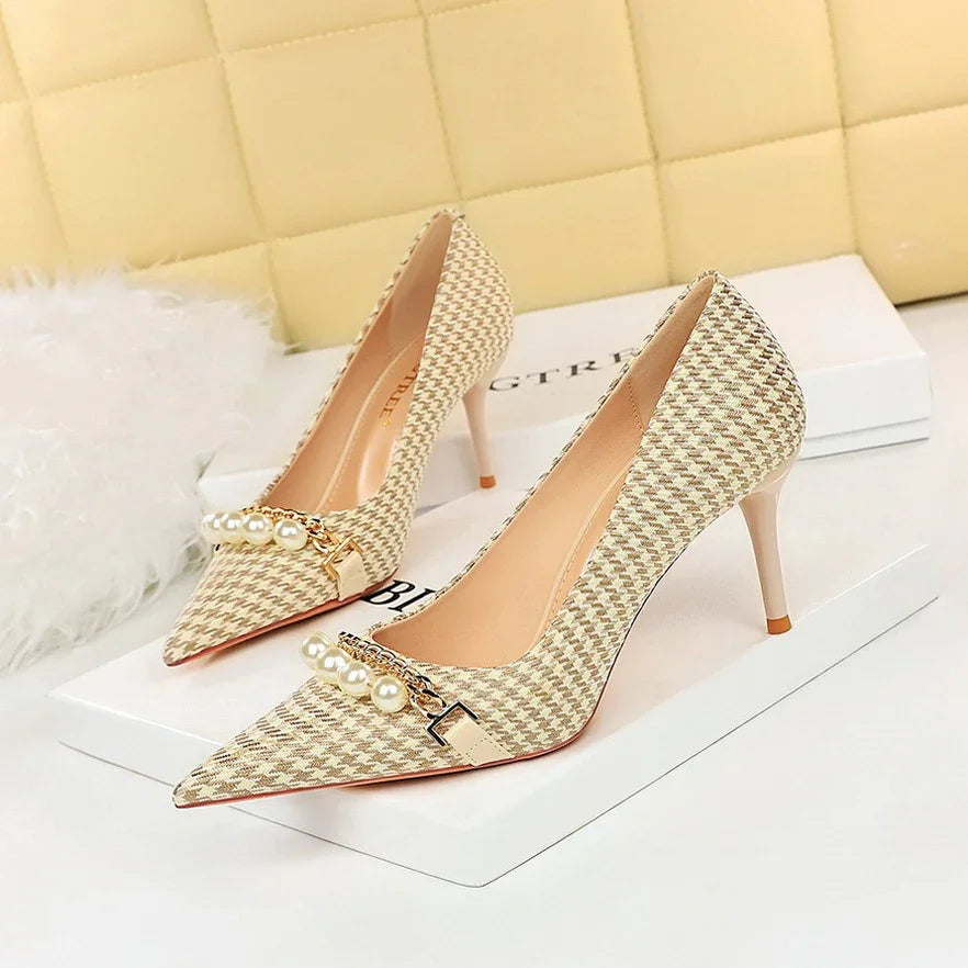 Elegant beige houndstooth high heels with pearl and gold chain embellishments on white boxes