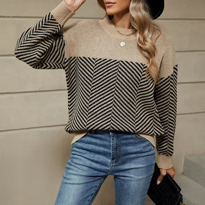 Woman wearing beige and black striped knit sweater with chevron pattern and blue jeans