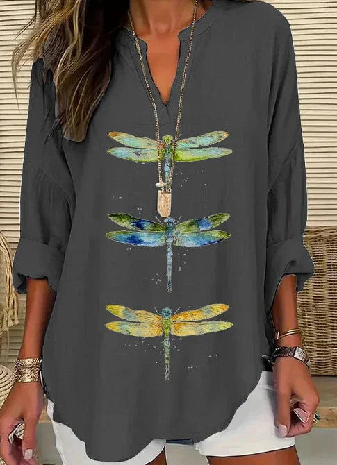 Woman wearing dark gray shirt with colorful dragonfly prints and gold accessories