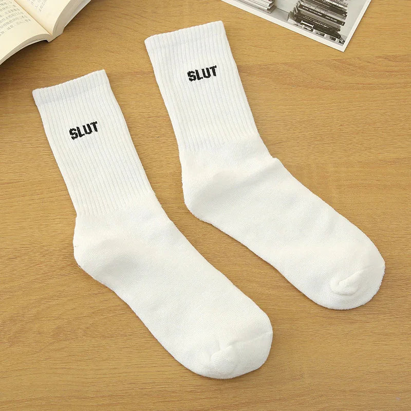 Pair of white ribbed crew socks with black embroidered text on a wooden surface