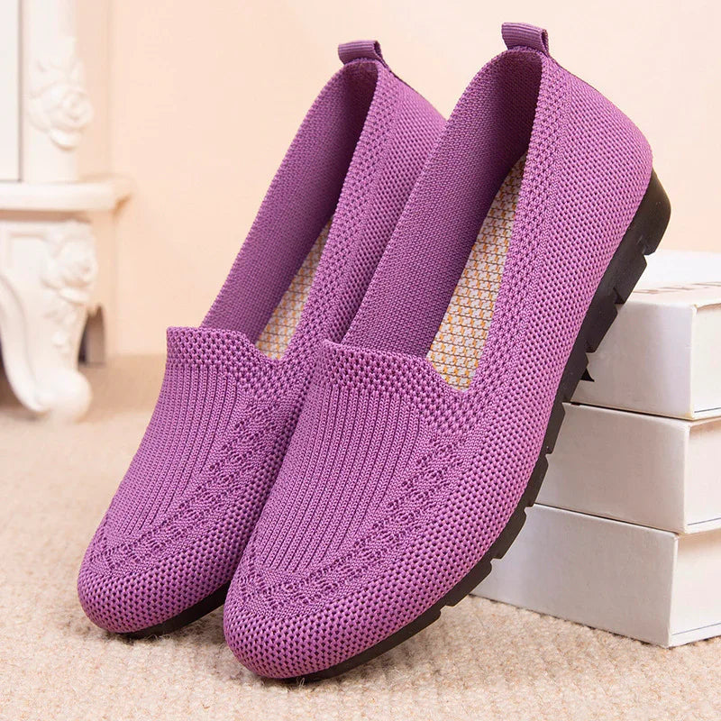 Pair of purple knit slip-on casual shoes with black soles on carpet near white boxes