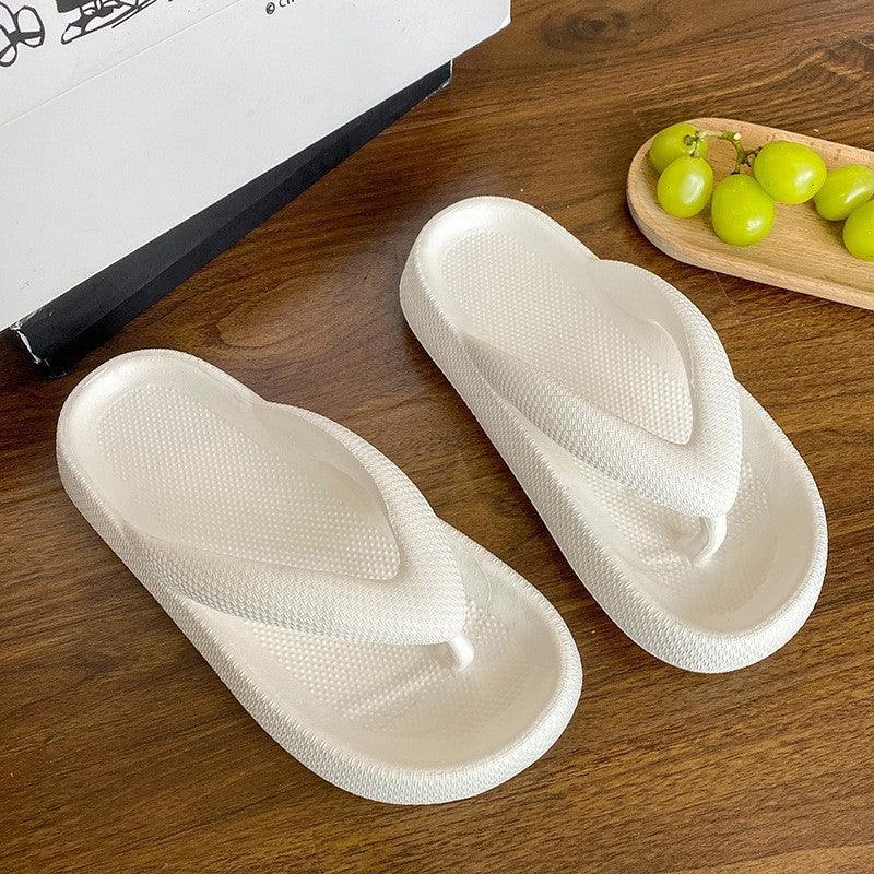 Pair of white textured foam flip-flop sandals on wooden surface with green grapes in wooden tray