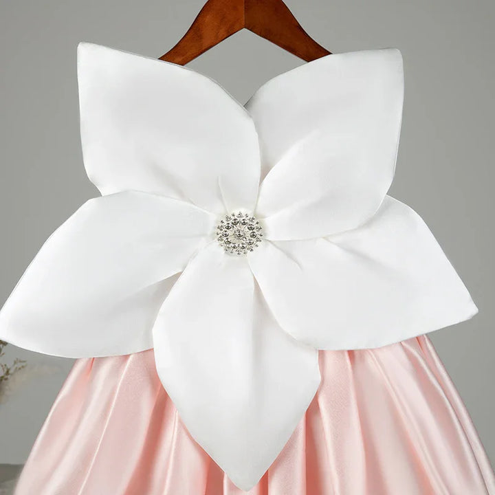 Pink satin dress with large white flower applique and jeweled center on wooden hanger