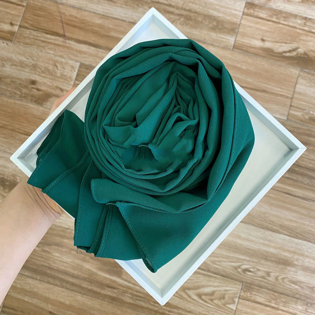 Hand holding a white tray with a neatly rolled emerald green chiffon fabric on light brown wooden floor