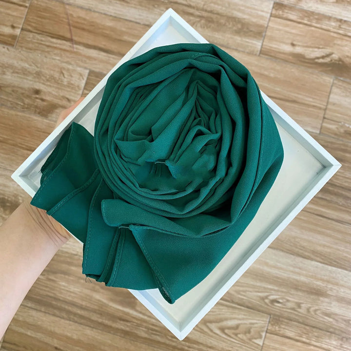 Hand holding a white tray with a neatly rolled emerald green chiffon fabric on light brown wooden floor