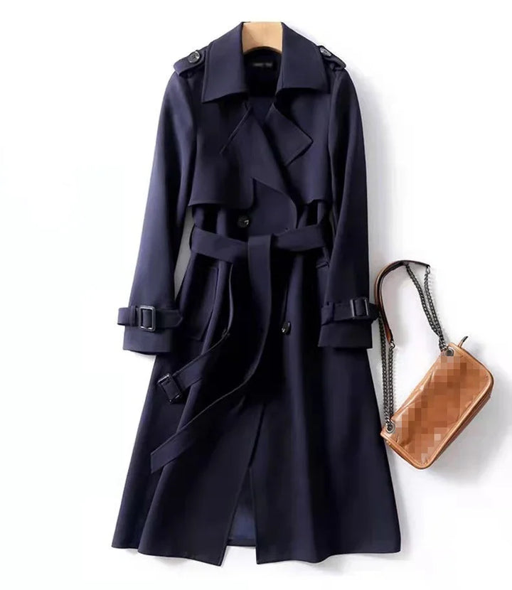Navy blue trench coat with belt and buckle details, paired with a tan handbag featuring chain straps