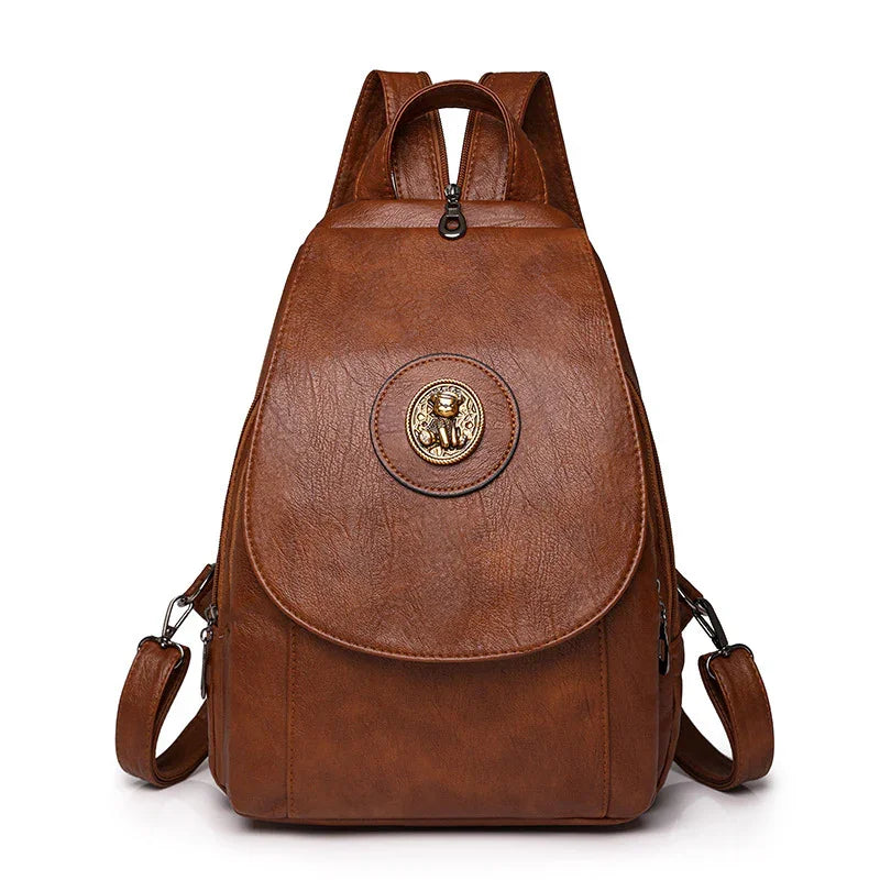 Brown leather backpack with round lion emblem and adjustable straps on white background