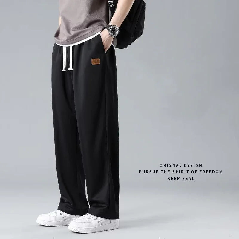 Casual black drawstring pants with leather patch label worn with white sneakers and watch on gray background