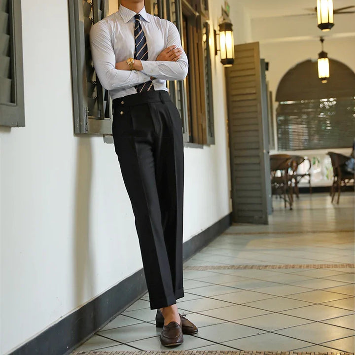 Man in formal black trousers, striped tie, and dress shirt leaning against wall in vintage indoor setting
