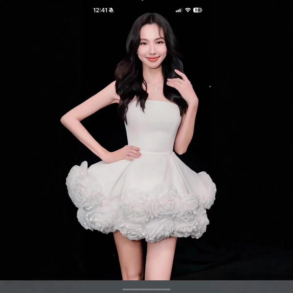 Woman in strapless white dress with 3D floral details posing against black background