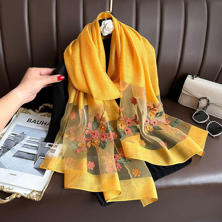 Yellow floral embroidered chiffon scarf draped on black fabric with white purse and sunglasses nearby