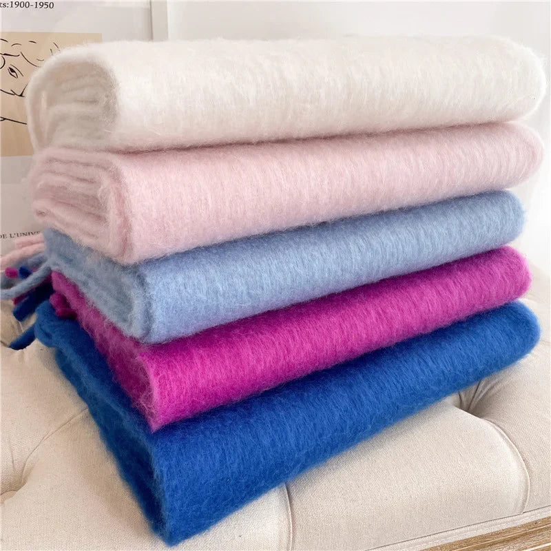 Stack of soft, fluffy scarves in cream, light pink, light blue, magenta, and royal blue on beige surface