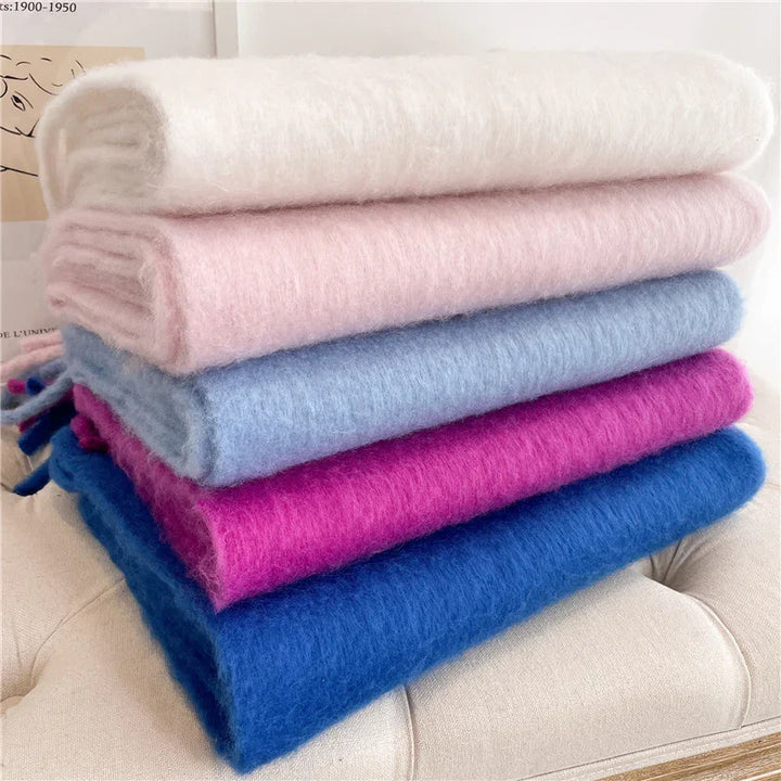 Stack of soft, fluffy scarves in cream, light pink, light blue, magenta, and royal blue on beige surface