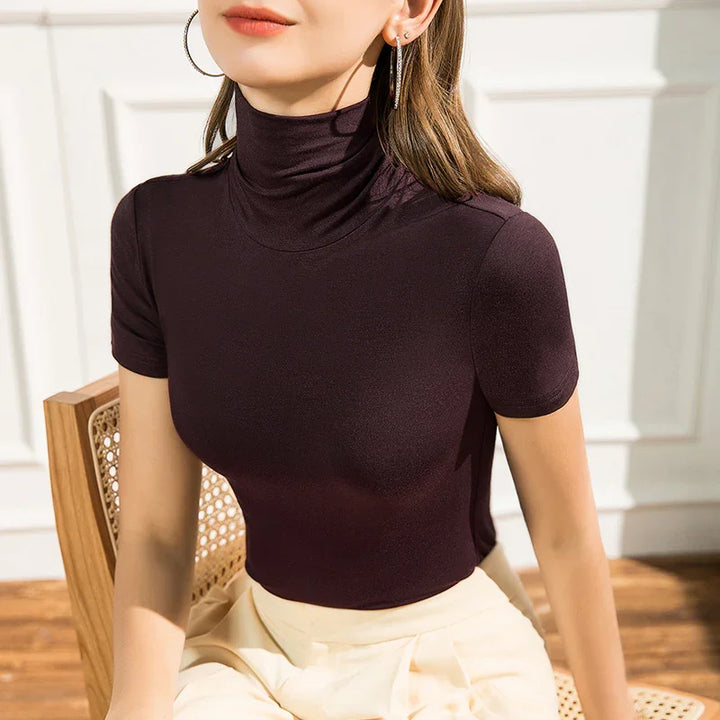 Woman wearing a fitted short-sleeve black turtleneck top sitting on a wooden chair in bright natural light