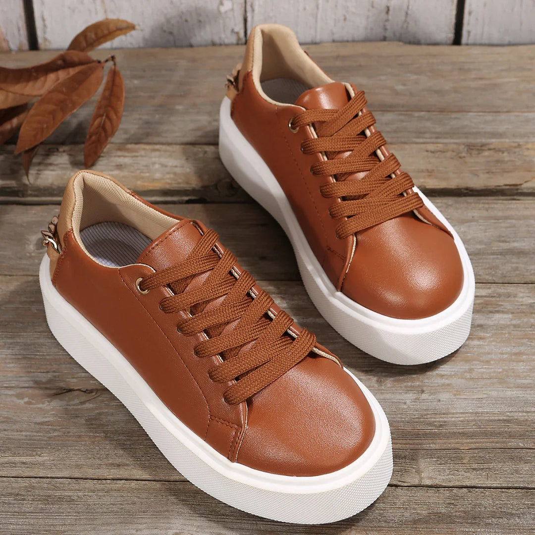 Pair of brown leather platform sneakers with thick white soles on rustic wooden surface