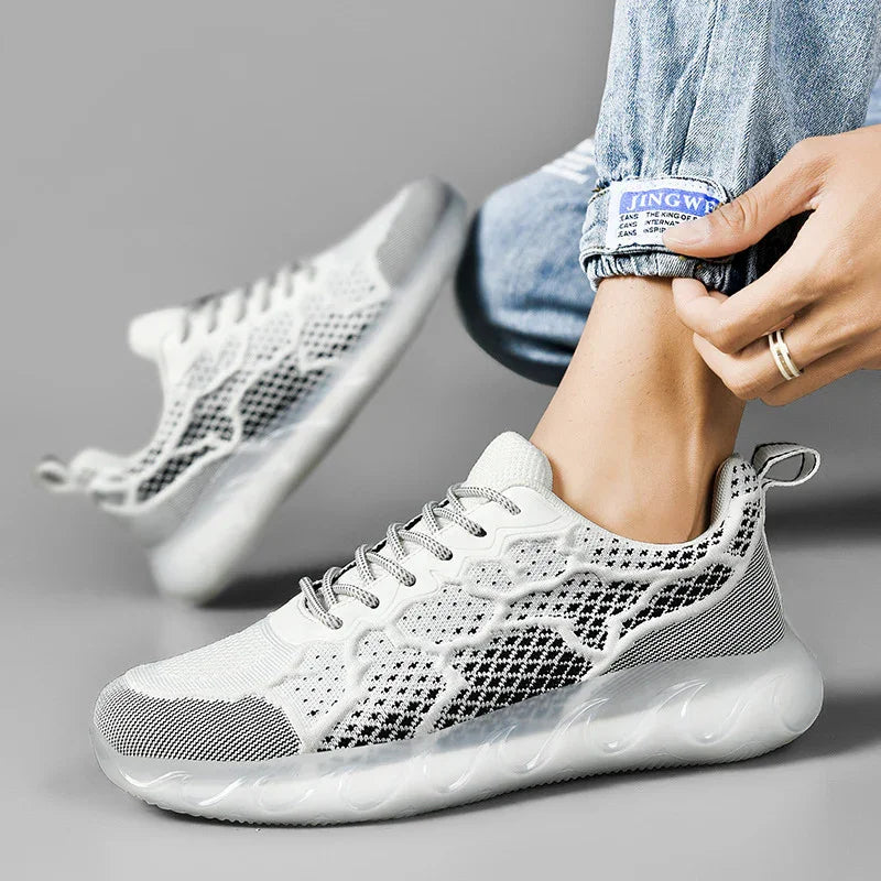 White and black knitted sneakers with transparent sole worn with rolled-up blue jeans on gray background