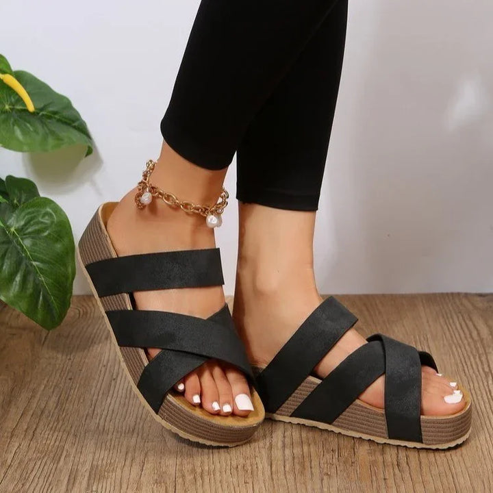 Woman wearing black crisscross strap platform sandals with gold pearl anklet on wooden floor