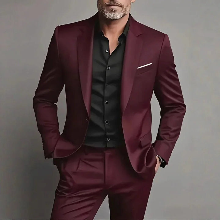 Man wearing stylish burgundy suit with black shirt and white pocket square against gray background
