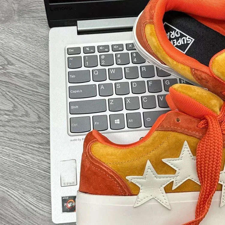 Orange and yellow suede sneakers with white star patches on a laptop keyboard