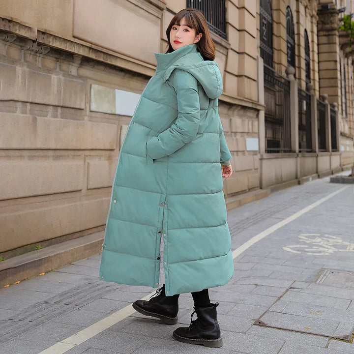 Woman wearing a long teal puffer coat and black boots walking on urban sidewalk