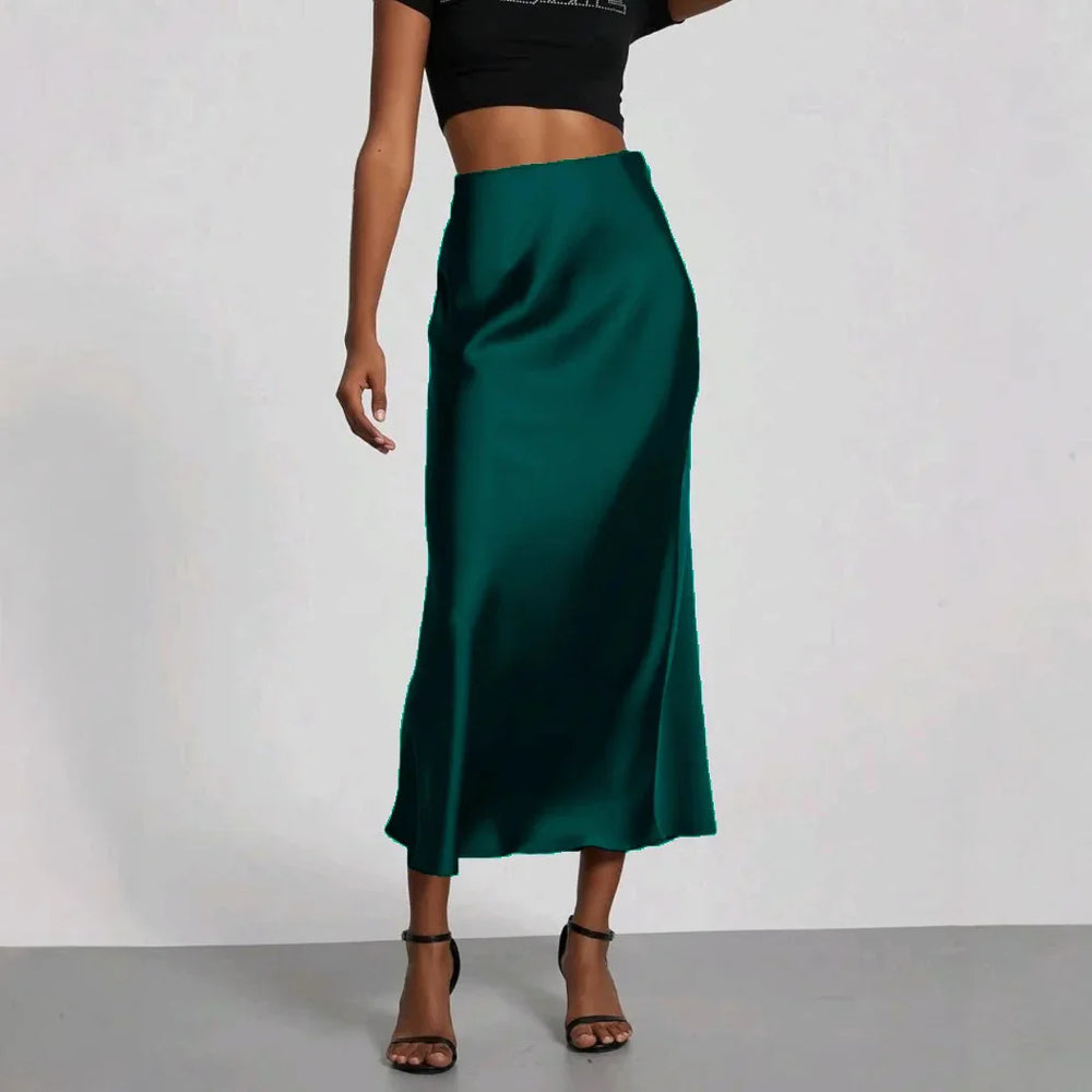 Woman wearing a high-waisted dark green satin midi skirt paired with black strappy heels and a black crop top