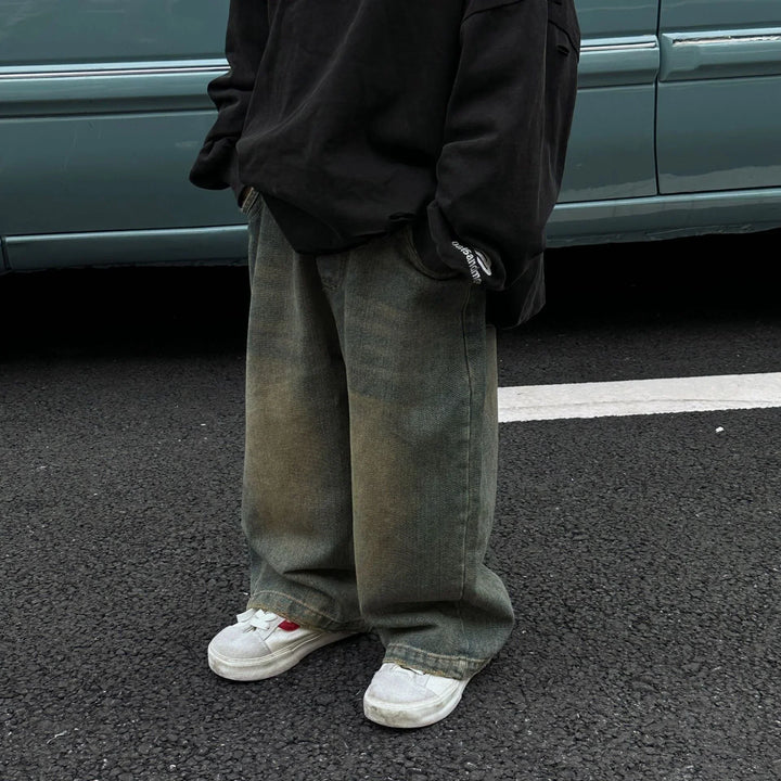 Person wearing baggy distressed jeans, black sweatshirt, and white sneakers standing on asphalt near light blue car