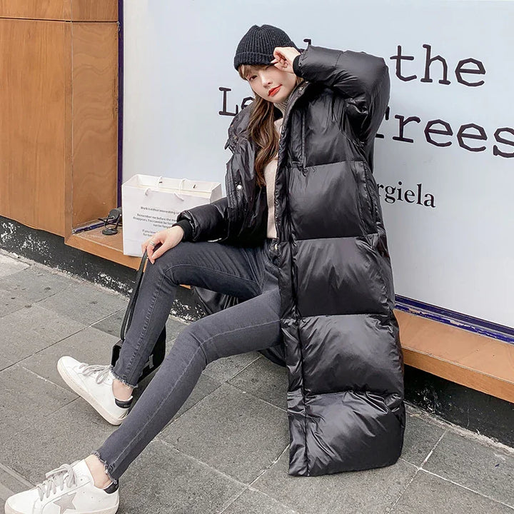 Woman in long black puffer coat, grey jeans, white sneakers, and black beanie sitting on street curb