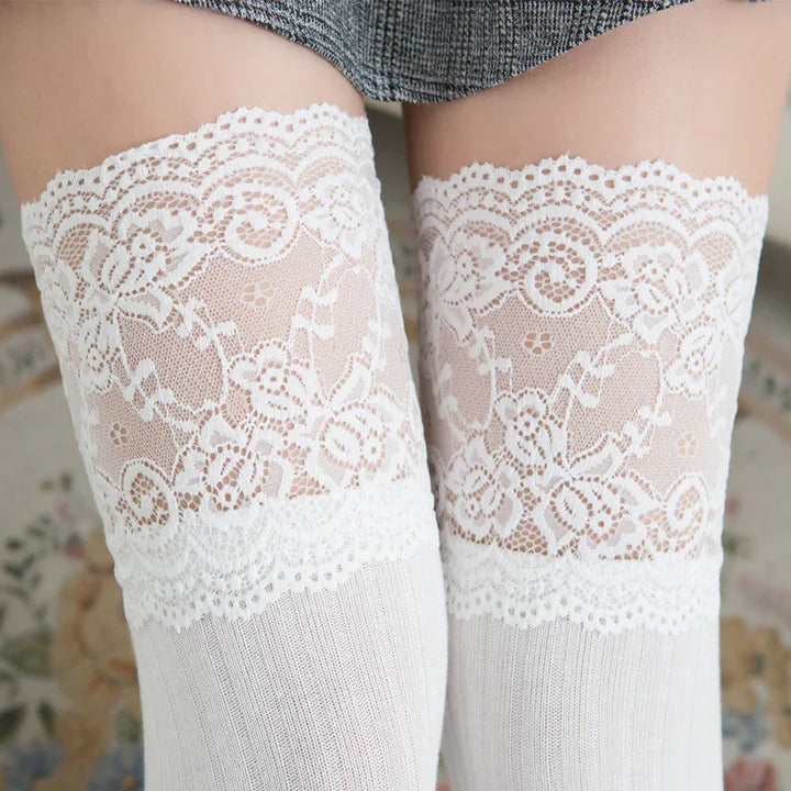 Close-up of white lace thigh-high stockings with floral patterns worn under gray skirt