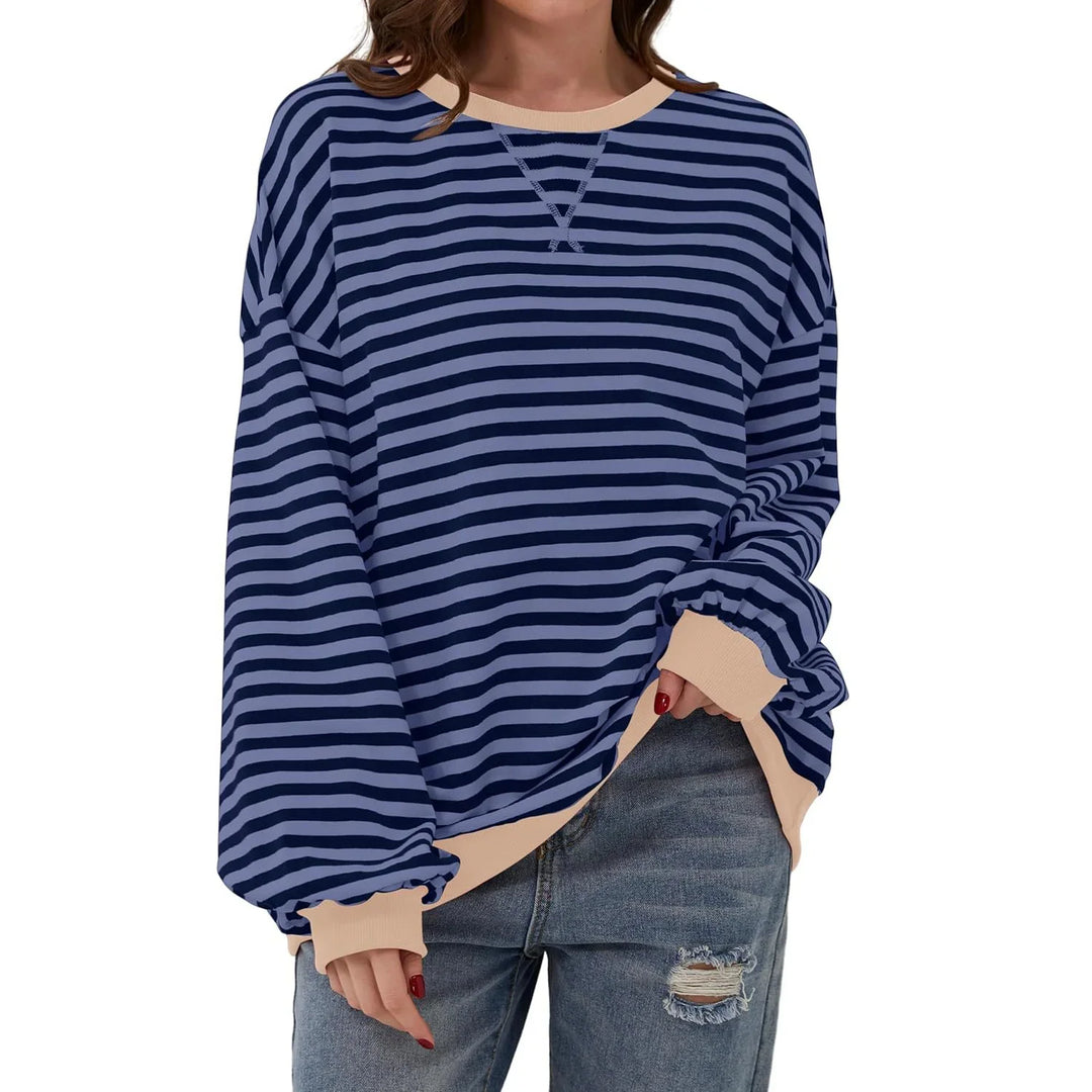 Woman wearing blue and navy striped long sleeve sweater with beige cuffs and neckline, paired with ripped jeans