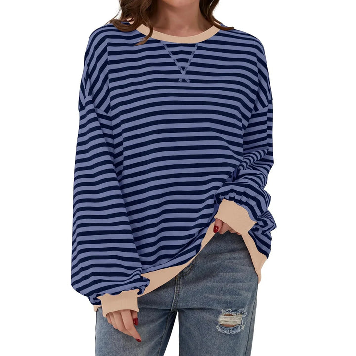 Woman wearing blue and navy striped long sleeve sweater with beige cuffs and neckline, paired with ripped jeans