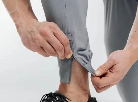 Close-up of hands adjusting zipper on gray athletic pants near black running shoe