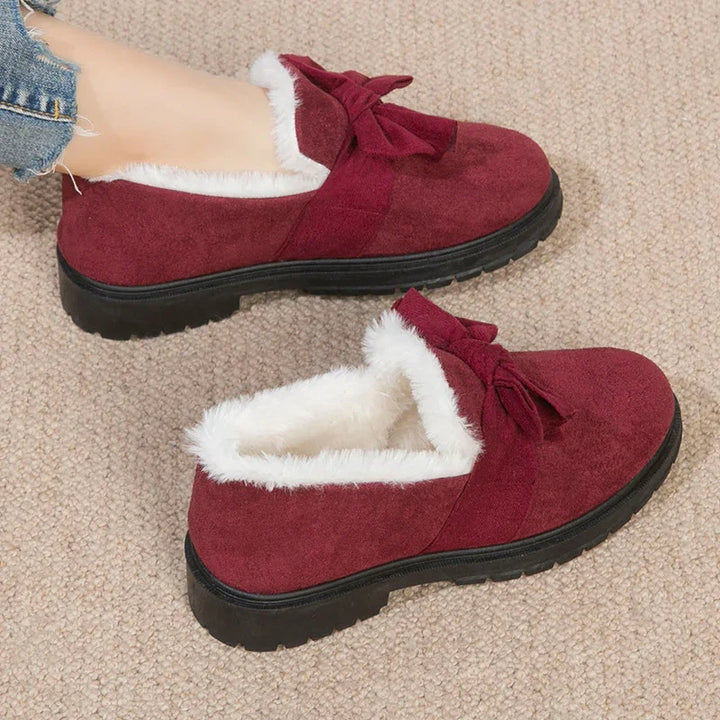 Burgundy suede winter shoes with white fur lining and bow detail on textured carpet