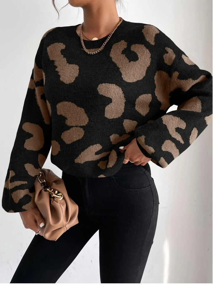 Woman wearing black and brown leopard print sweater with black pants holding a beige clutch bag