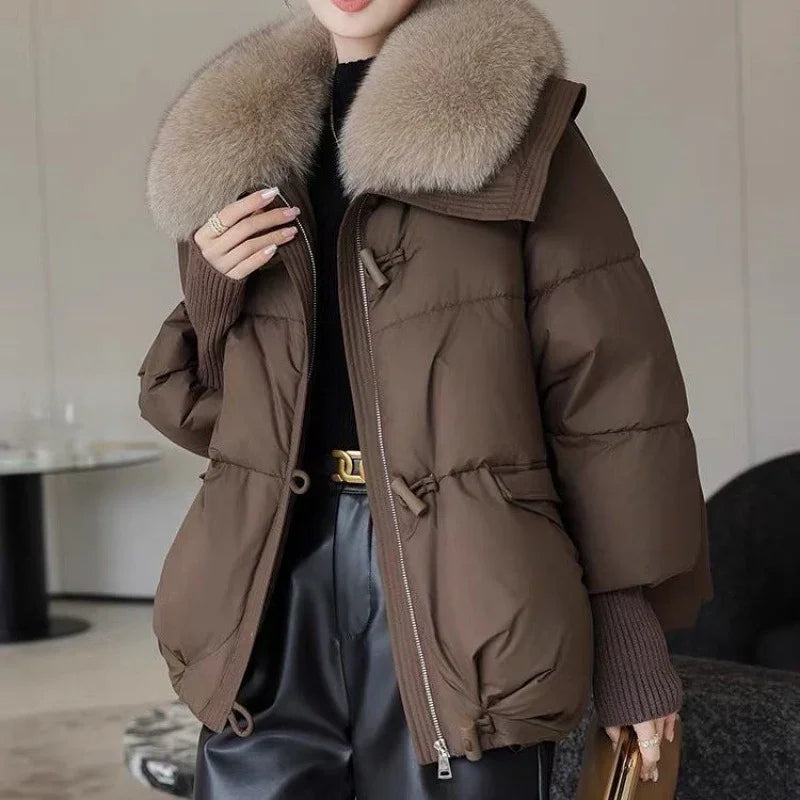 Woman wearing brown puffer jacket with large beige fur collar and black leather pants indoors