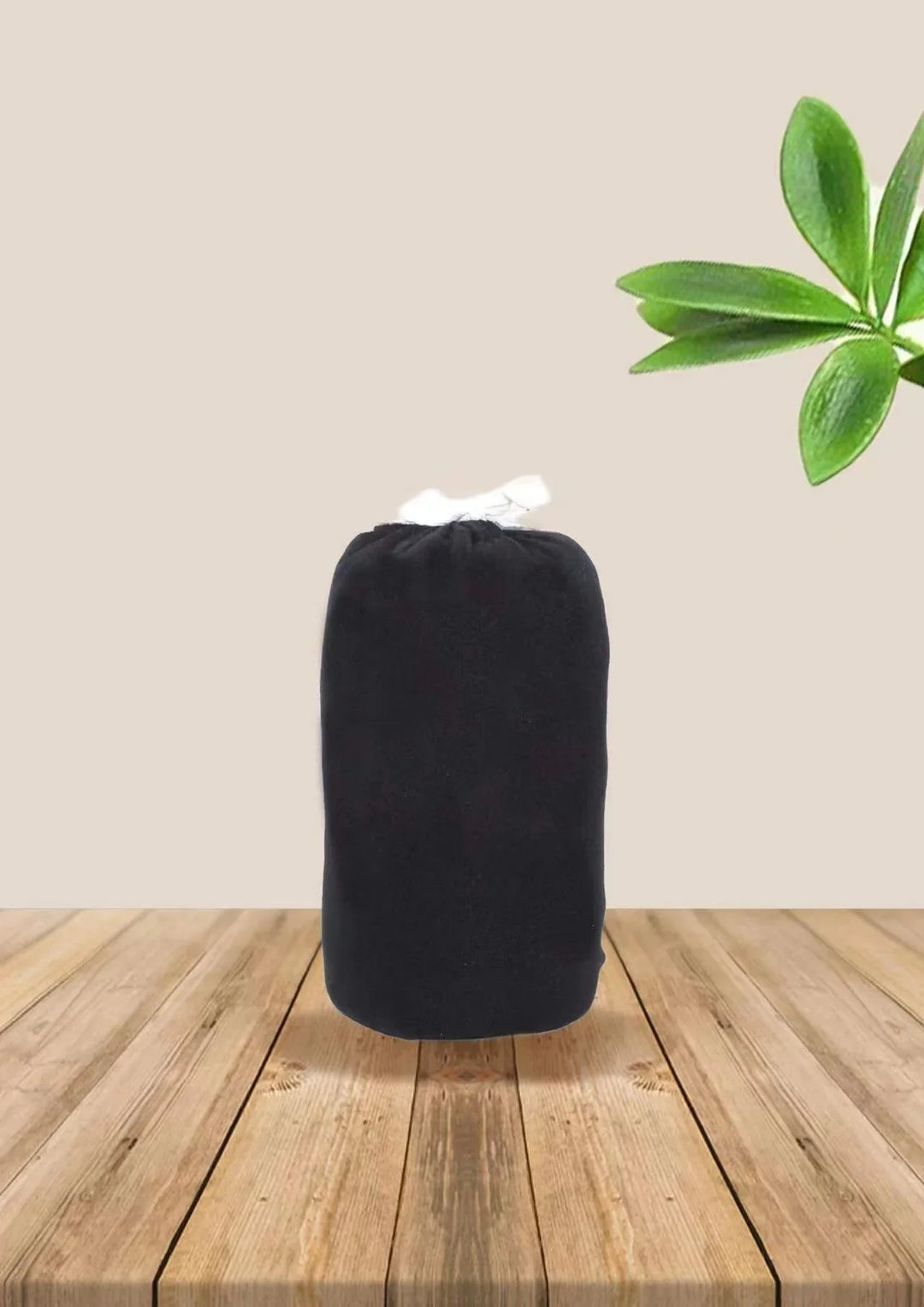 Black drawstring bag on wooden surface with green leaves on beige background