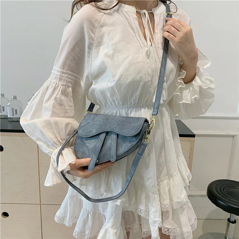 Woman wearing white ruffled dress holding blue suede crossbody bag indoors
