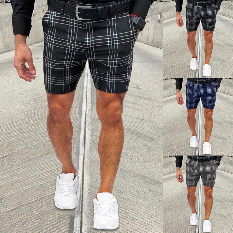 Man wearing black, blue, and grey plaid shorts with white sneakers on concrete pavement