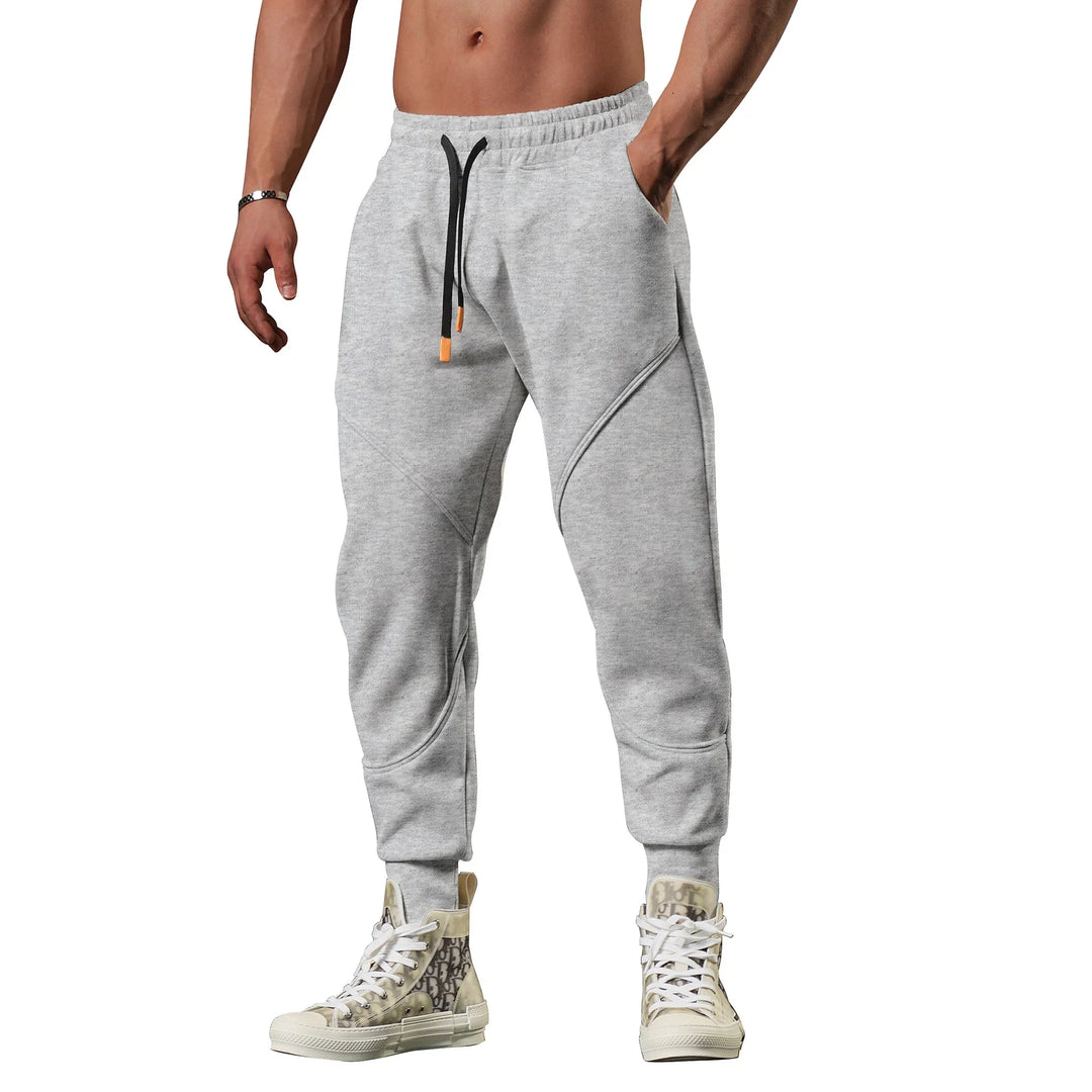 Man wearing light grey jogger sweatpants with black drawstrings and patterned high-top sneakers