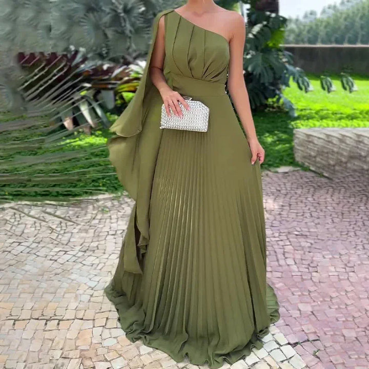 Woman wearing elegant olive green one-shoulder pleated evening gown holding silver clutch outdoors