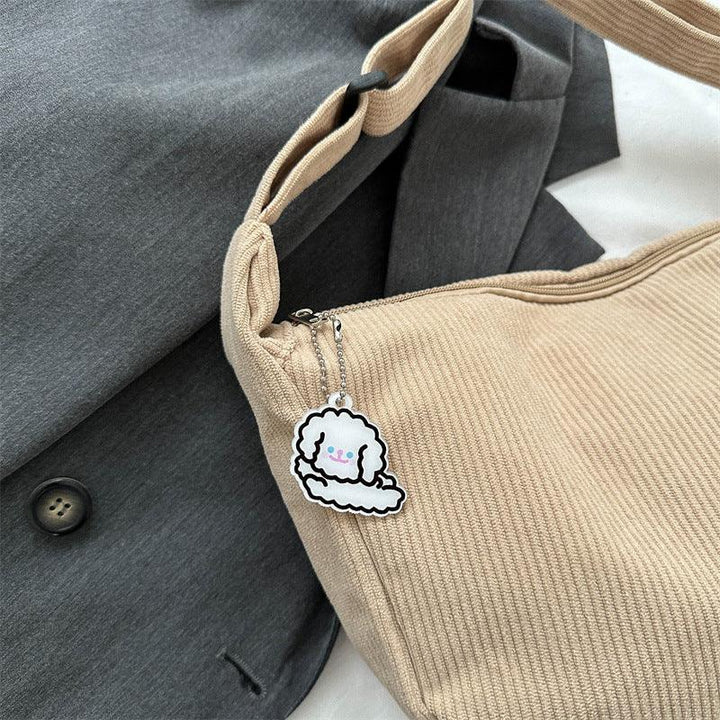 Beige ribbed fabric bag with cute white dog keychain attached, placed on gray blazer